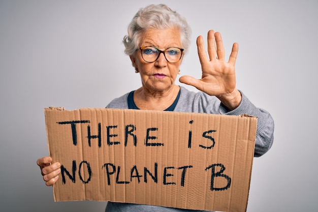 Una anciana hermosa de pelo gris que pide un medio ambiente sosteniendo una pancarta con un mensaje de la tierra con la mano abierta haciendo una señal de stop con un gesto de defensa de expresión seria y segura