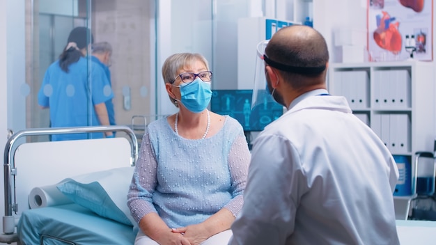 Anciana jubilada con máscara en consulta médica durante la pandemia de COVID-19. Sistema de salud, tratamiento de enfermedades en una clínica u hospital privado profesional moderno