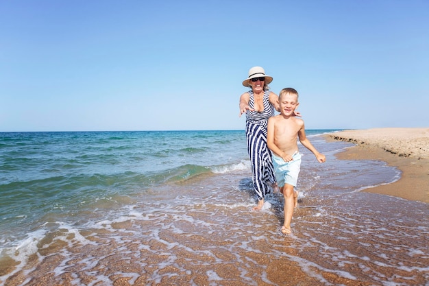 Una anciana juega con un niño a la orilla del mar La abuela y el nieto riéndose corren por la playa de arena Amor y ternura Estilo de vida activo salud y relajación en el resort