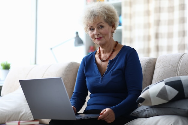Anciana con laptop está sentada en el sofá