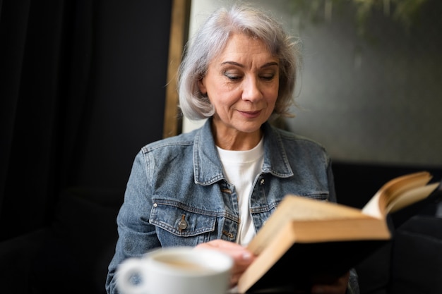 Anciana leyendo un libro y tomando café en un café