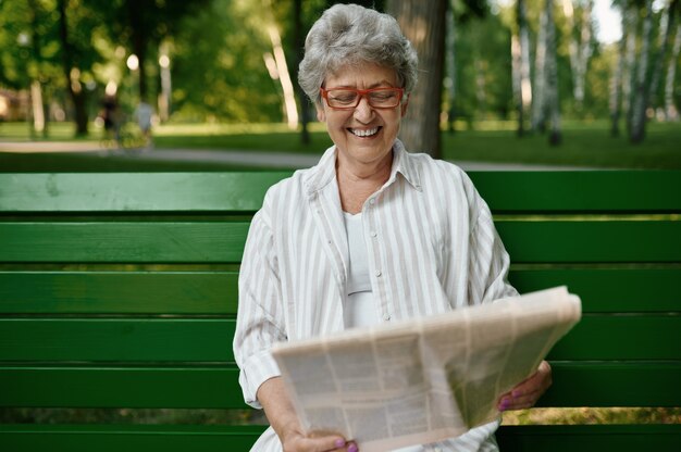 Una anciana leyendo el periódico en el banquillo.