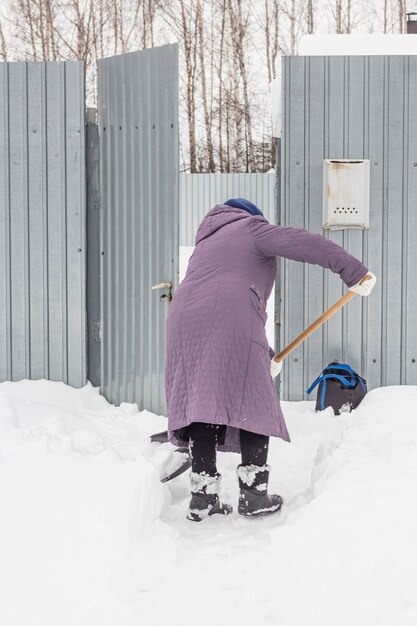 Una anciana limpia la nieve cerca de su casa en el pueblo