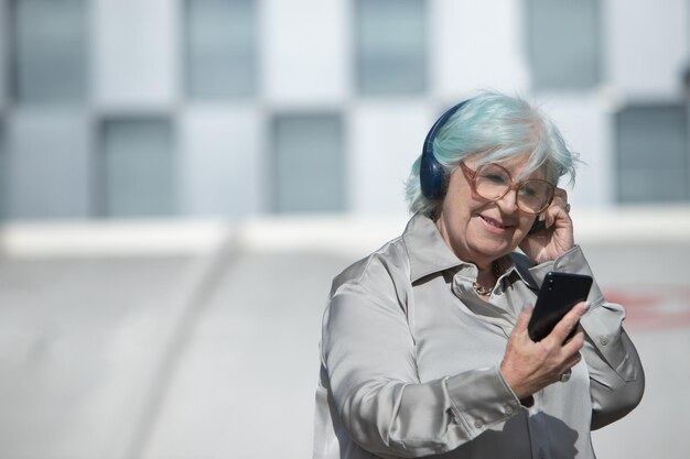 Anciana mirando la pantalla del teléfono celular con auriculares al aire libre