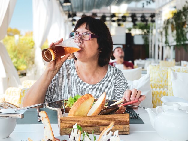 Anciana morena bebiendo cerveza en un restaurante