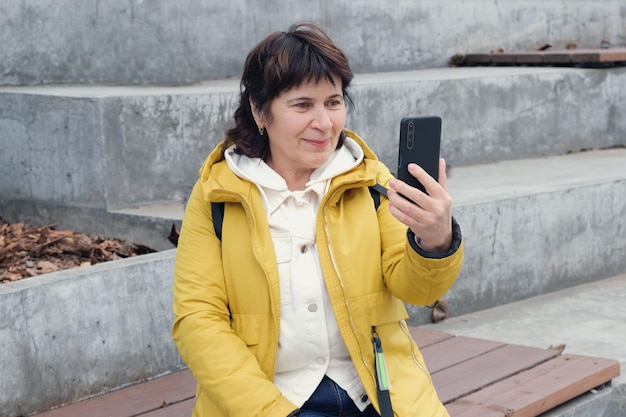 Una anciana morena se sienta en un parque de la ciudad en los escalones sonriendo mientras habla por un enlace de video