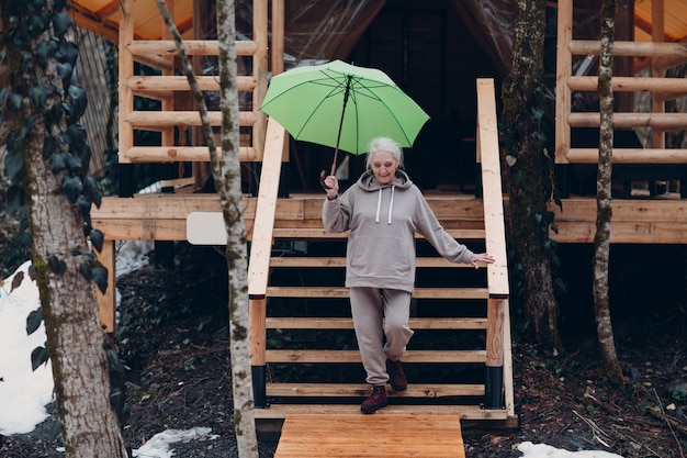 Anciana mujer madura con paraguas en la tienda de campaña glamping. Concepto de estilo de vida moderno de vacaciones.