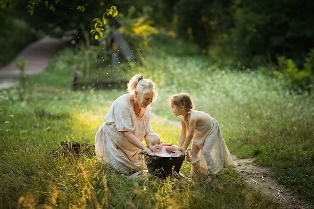 Anciana y niña bañan a un bebé en una cuenca al aire libre