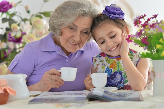 Anciana con una niña bebiendo té y leyendo una revista