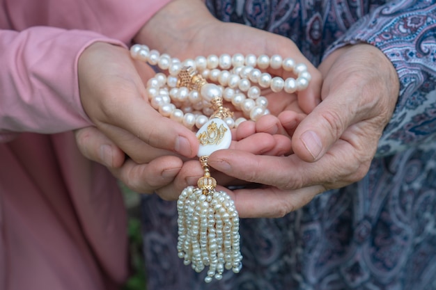 Una anciana y una niña sostienen un hermoso rosario blanco. Manos de una anciana y una niña con primer plano de rosario de perlas. Concepto religioso.