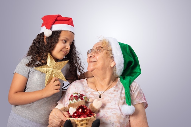 Anciana y niño con sombrero de Navidad y adornos navideños en manos en gris