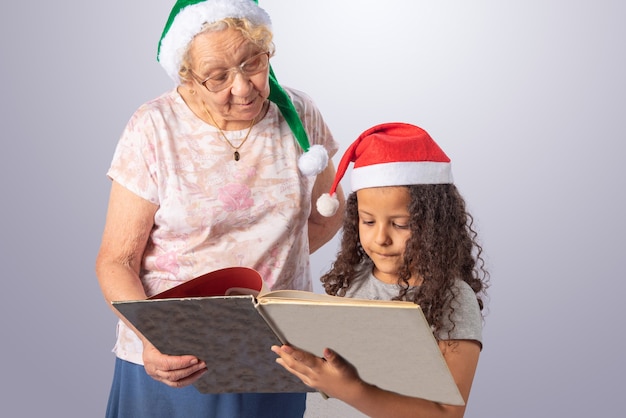 Anciana y niño con sombrero de Navidad leyendo un libro en gris