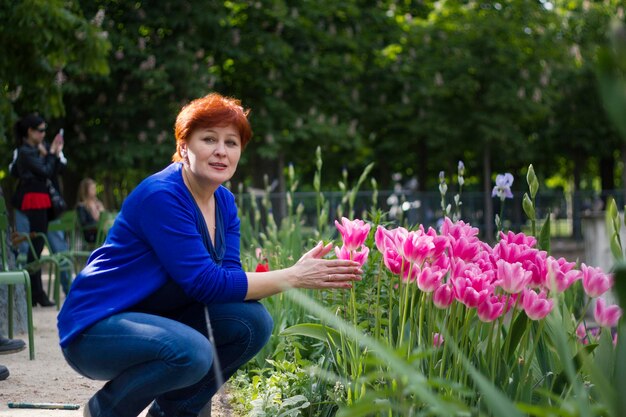 Una anciana en un parque cerca de las flores, toca los pétalos.