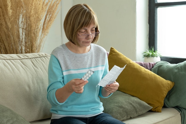 Una anciana con pastillas lee las instrucciones en casa sentada en el sofá