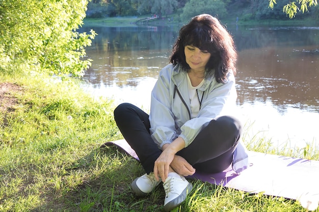 Una anciana pensativa con ropa deportiva se sienta en un parque a orillas del río