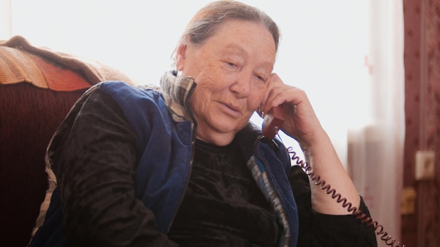 Anciana pensionista hablar teléfono fijo y sonriendo, de cerca, telefoto