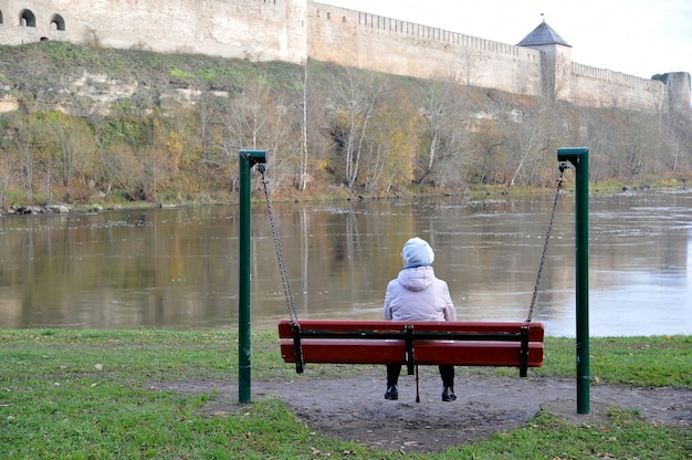 Una anciana pensionista sentada en un banco y mirando el río y la antigua fortaleza