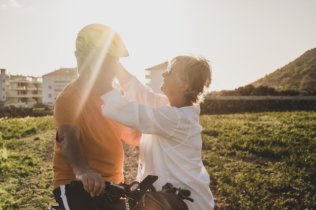 La anciana le pone un casco protector a su esposo para andar en bicicleta Luz brillante del atardecer