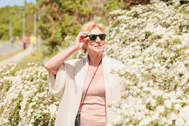 Anciana posando entre arbustos con flores blancas