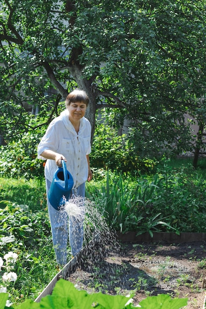 Una anciana regando las plantas en el jardín.