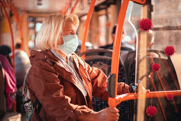 Anciana rubia adulta vistiendo una máscara protectora médica en transporte público