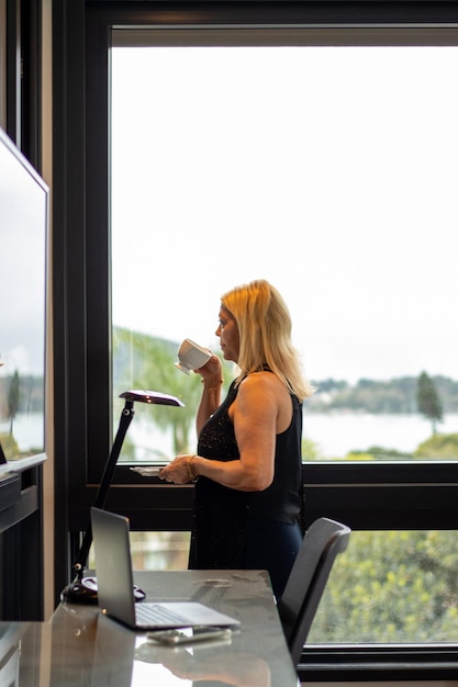 anciana rubia tomando un café y mirando por la ventana de su dormitorio