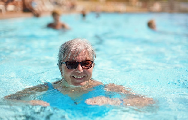 Anciana senior con cabello gris, vistiendo traje de baño azul sonriendo en la piscina del hotel