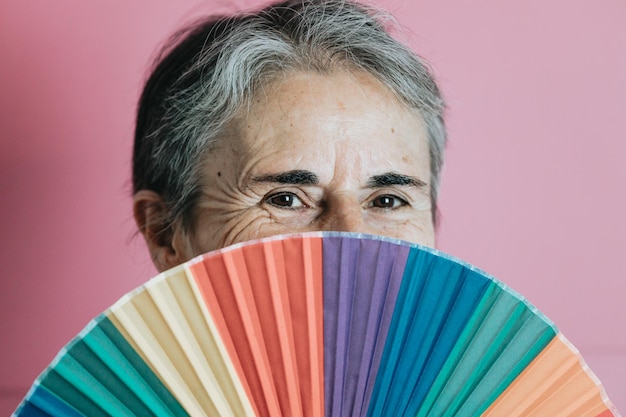 Anciana senior de pelo blanco sosteniendo un abanico de mano lgbti de colores de fondo. Concepto senior de personas mayores. Derechos de la mujer fondo morado amistoso lgbt