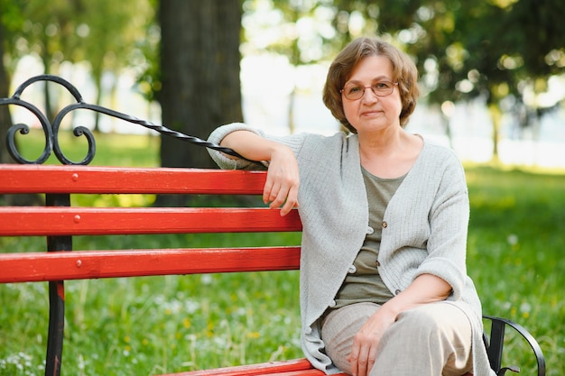 Una anciana sentada en un banco en el parque de verano