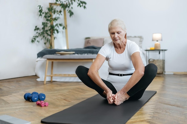 Anciana sentada en una pose de yoga frente a una computadora portátil abierta