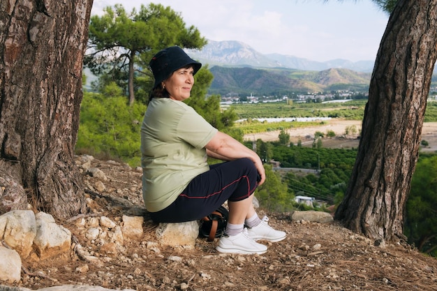 Anciana se sienta en una piedra y descansa durante un viaje de senderismo