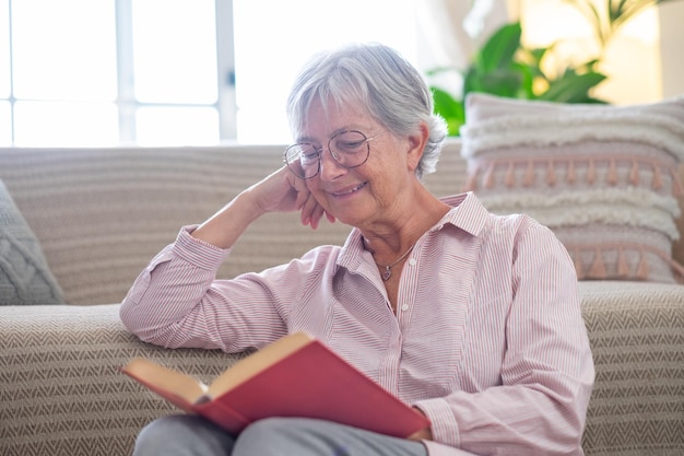 Una anciana sonriente y atractiva relajándose sentada en el suelo leyendo un libro Señora madura caucásica estudiando aprendiendo en casa