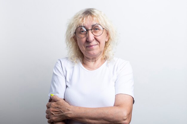 Anciana sonriente en una camiseta blanca con gafas sobre un fondo claro.