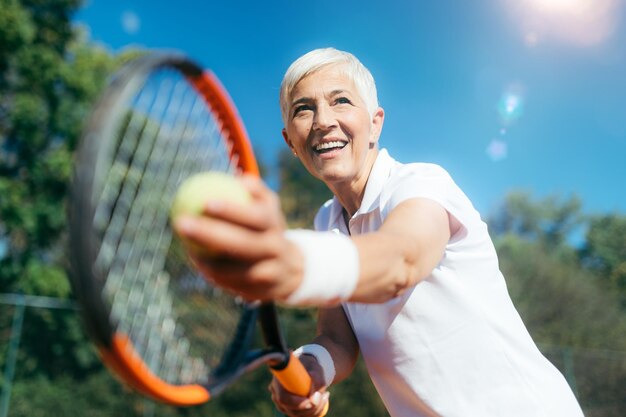 Anciana sonriente jugando tenis como actividad recreativa