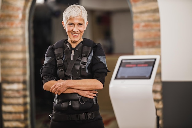 Una anciana sonriente posa antes del entrenamiento EMS en el gimnasio. Mirando a la cámara.