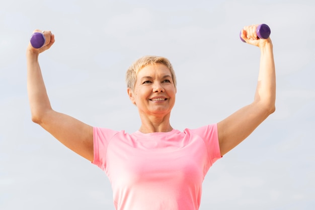 Anciana sonriente sosteniendo pesas mientras hace ejercicio