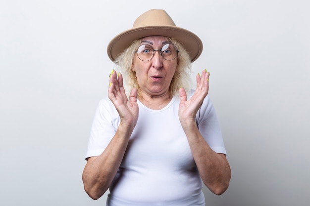 Foto anciana sorprendida con un sombrero sobre un fondo claro.