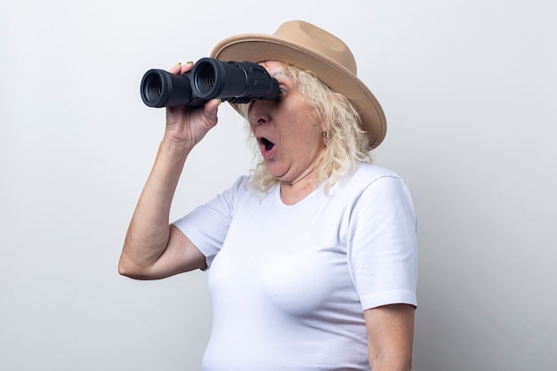 Anciana sorprendida sosteniendo binoculares sobre un fondo claro.