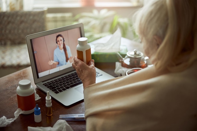 Anciana sosteniendo pastillas y hablando con el médico a través de una videollamada