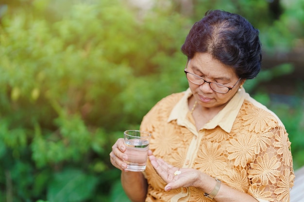 Una anciana tailandesa se sienta y mira la píldora en su mano con un vaso de agua para comer