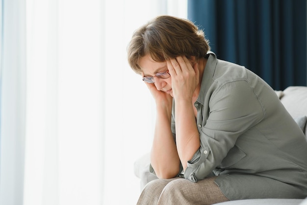 Una anciana tiene dolores de cabeza, se toca la cabeza con las manos y reporta síntomas de mareos, migrañas