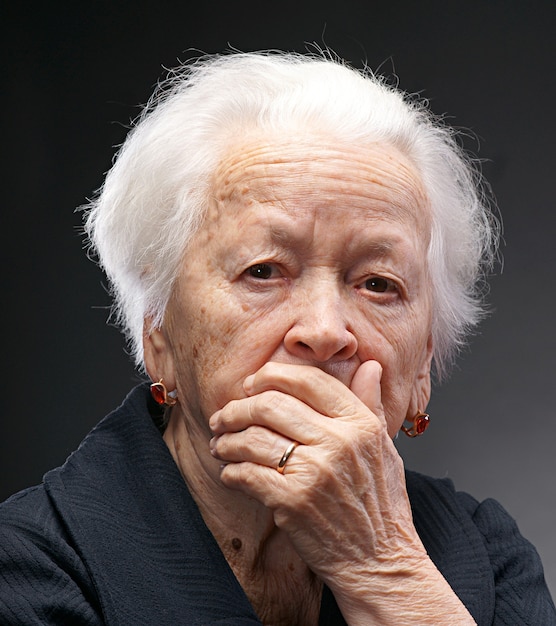 Anciana triste posando en estudio sobre fondo gris