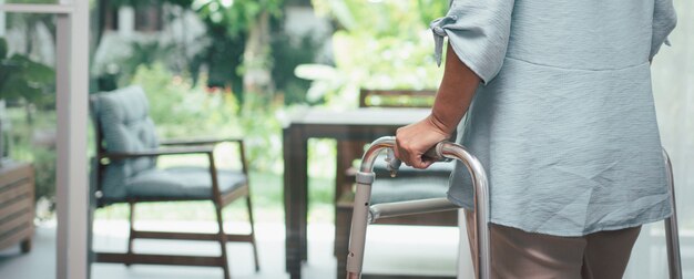 Una anciana triste usa Walker para pararse frente a las ventanas y mirar afuera