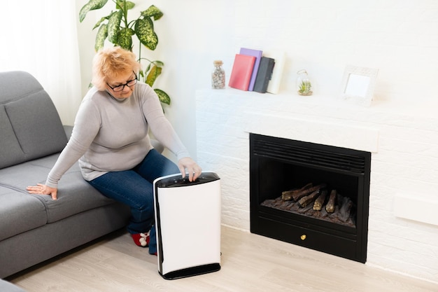 una anciana usa un purificador de aire en un apartamento mientras afuera hay una situación de contaminación del aire.