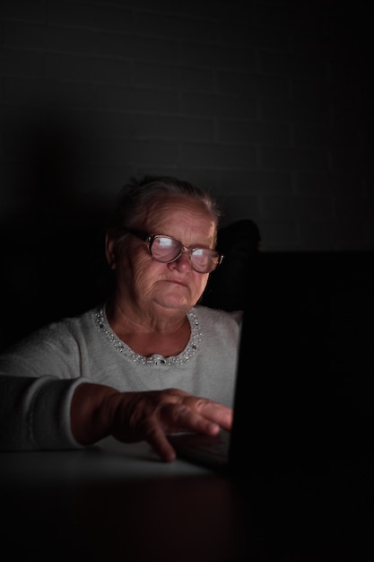 Anciana usando una computadora portátil en la oscuridad