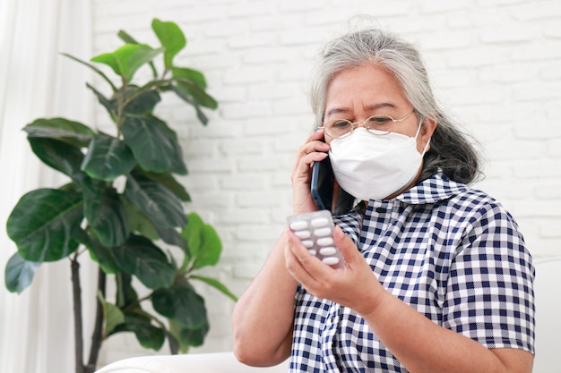 Ancianas asiáticas con máscaras. Habla con su médico en su teléfono inteligente sobre la medicación para su enfermedad. Cuidarse en casa durante la pandemia de COVID-19. aislamiento en casa