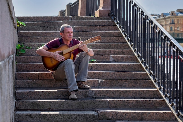 Un anciano adulto en edad de jubilación toca la guitarra acústica al aire libre