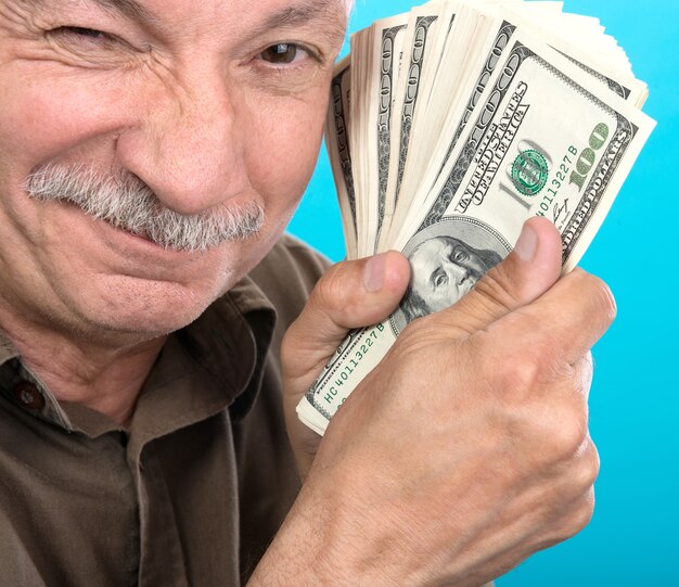 Anciano afortunado sosteniendo billetes de un dólar sobre un fondo azul.