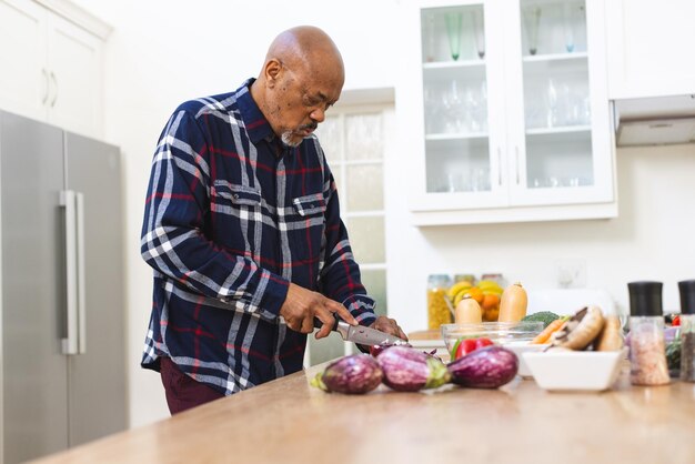 Un anciano afroamericano preparando verduras y cortando cebollas en la cocina.