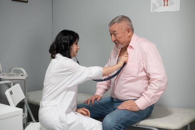 Un anciano al que el médico le revisa los latidos del corazón con un estetoscopio.